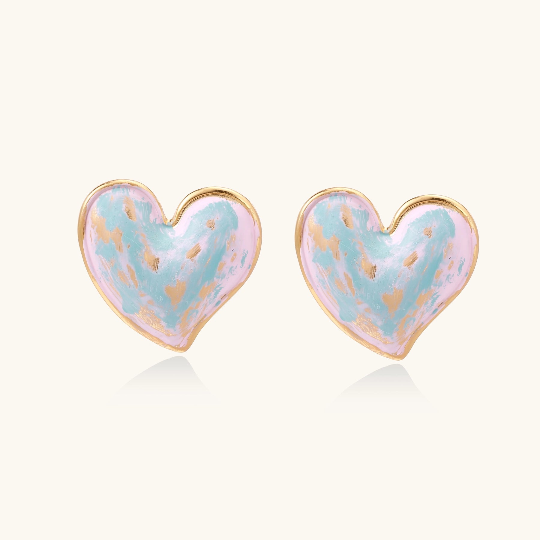 Heart-shaped stud earrings with swirled turquoise and pink enamel in gold-plated frames on cream background