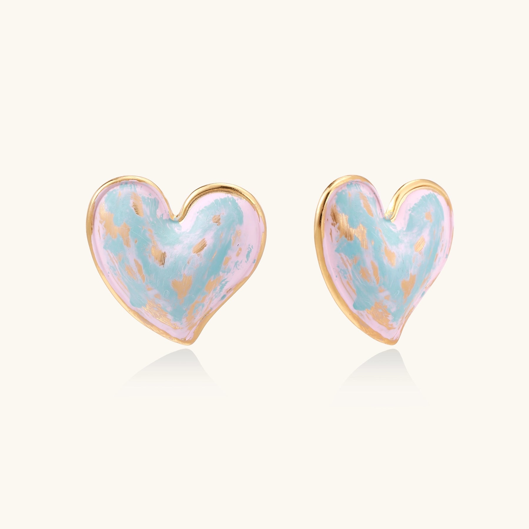 Heart-shaped stud earrings with swirled turquoise and pink enamel in gold-plated frames on cream background