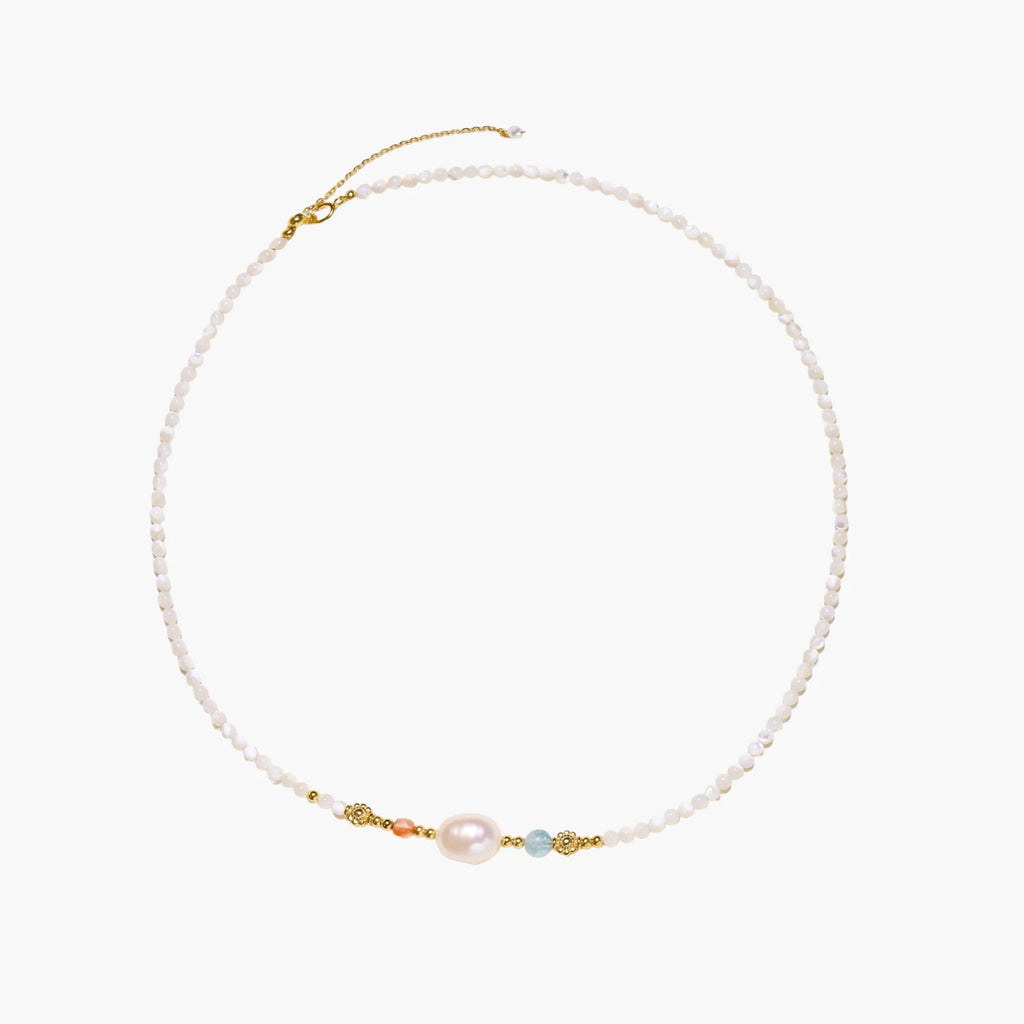 Delicate white beaded necklace with baroque pearl center, gold accents, and coral and aqua gemstones on cream background.