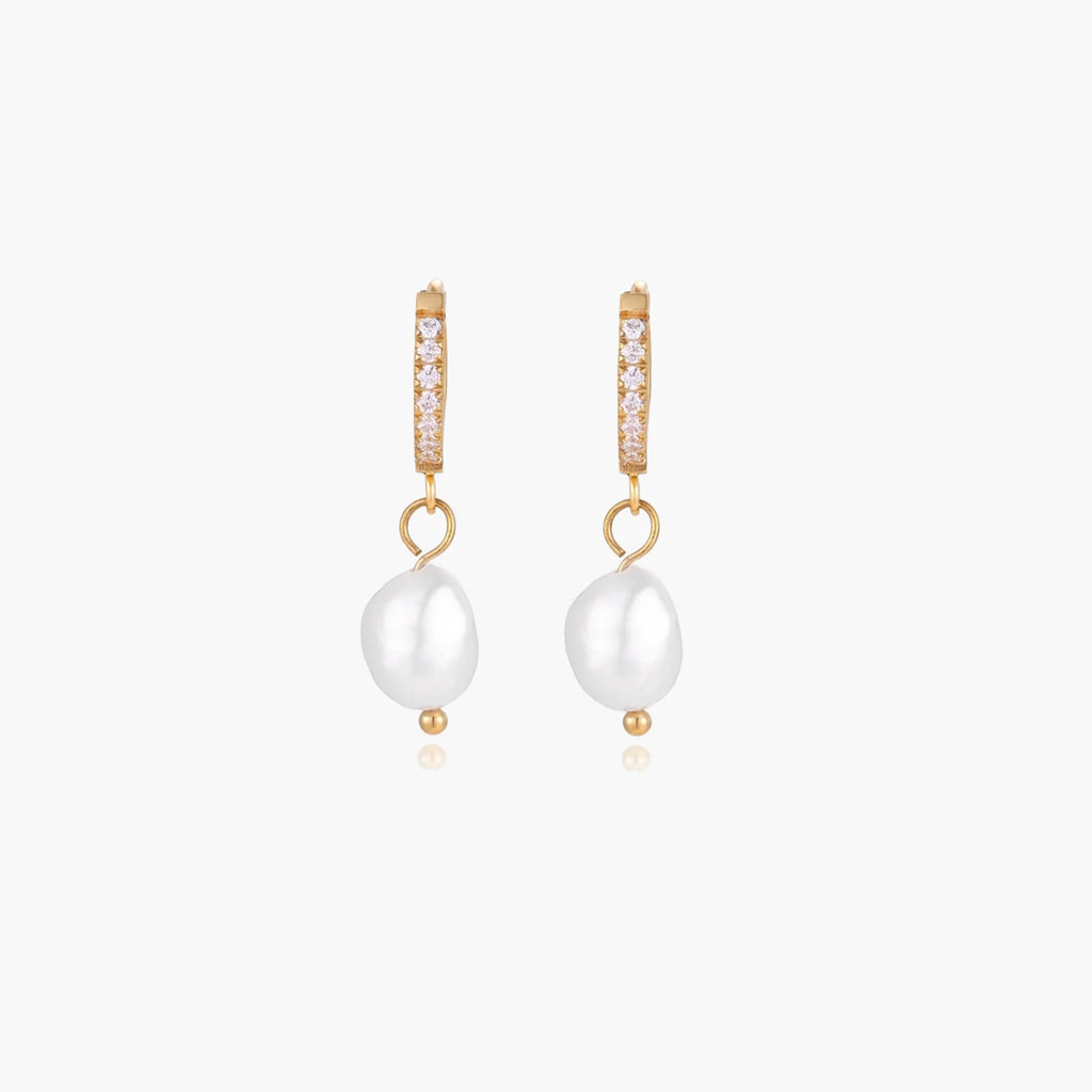 Gold huggie hoop earrings with pavé crystals and white freshwater pearl drops on cream background