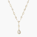 Y-shaped gold necklace with alternating geometric links, freshwater pearls, and baroque pearl pendant on cream background