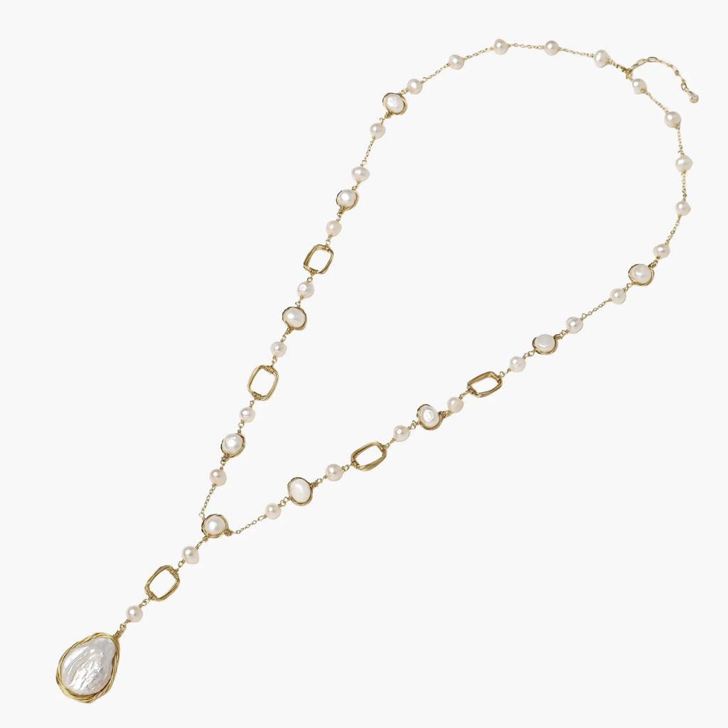 Y-shaped gold necklace with alternating geometric links, freshwater pearls, and baroque pearl pendant on cream background