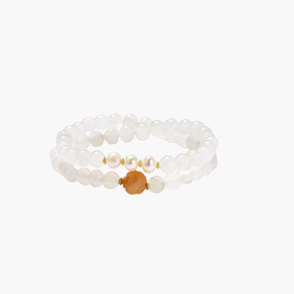 Three layered white beaded bracelets with carved orange agate lotus centerpiece and freshwater pearls on cream background.