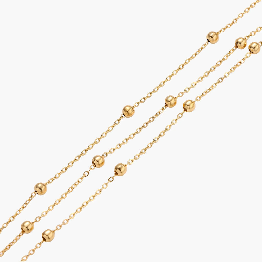 Three-strand gold-plated bracelet with clustered ball beads and adjustable clasp on cream background
