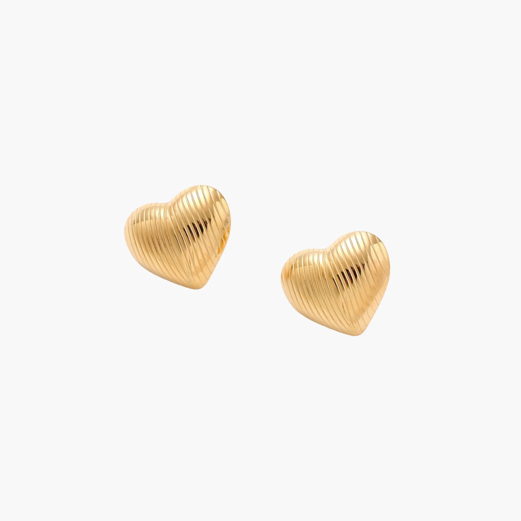 Gold heart-shaped stud earrings with parallel ridged texture on cream background