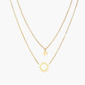 Gold layered necklace set with sunburst and smiley face pendants on delicate chains against white background.