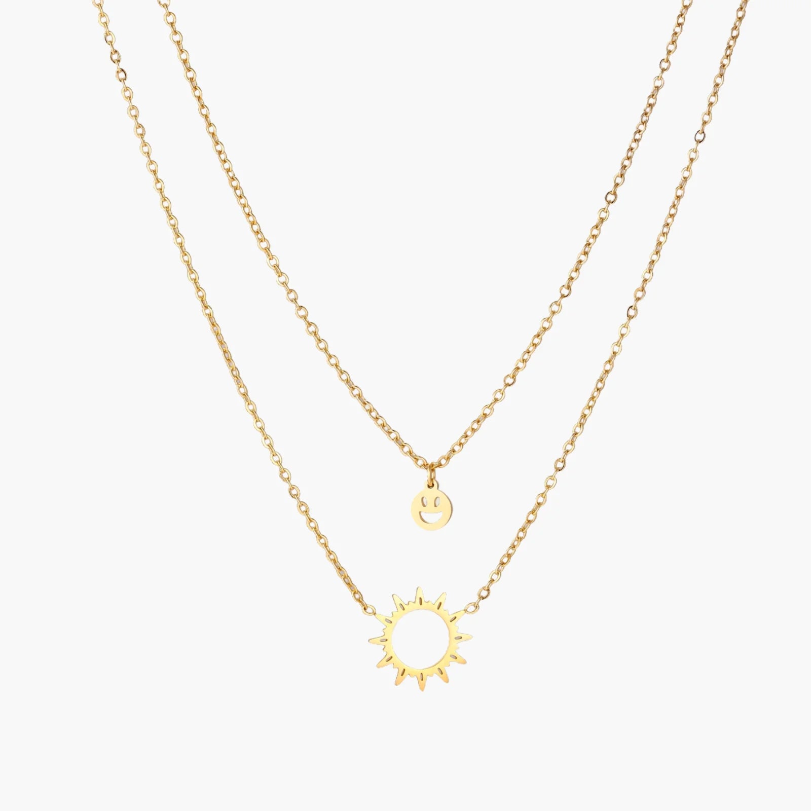 Gold layered necklace set with sunburst and smiley face pendants on delicate chains against white background.
