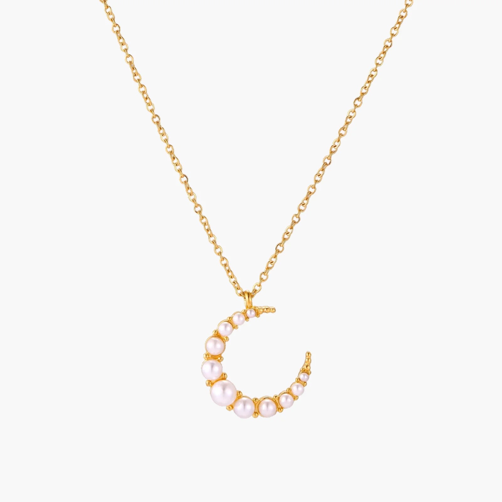 Gold crescent moon pendant with graduated white pearls on delicate chain against cream background