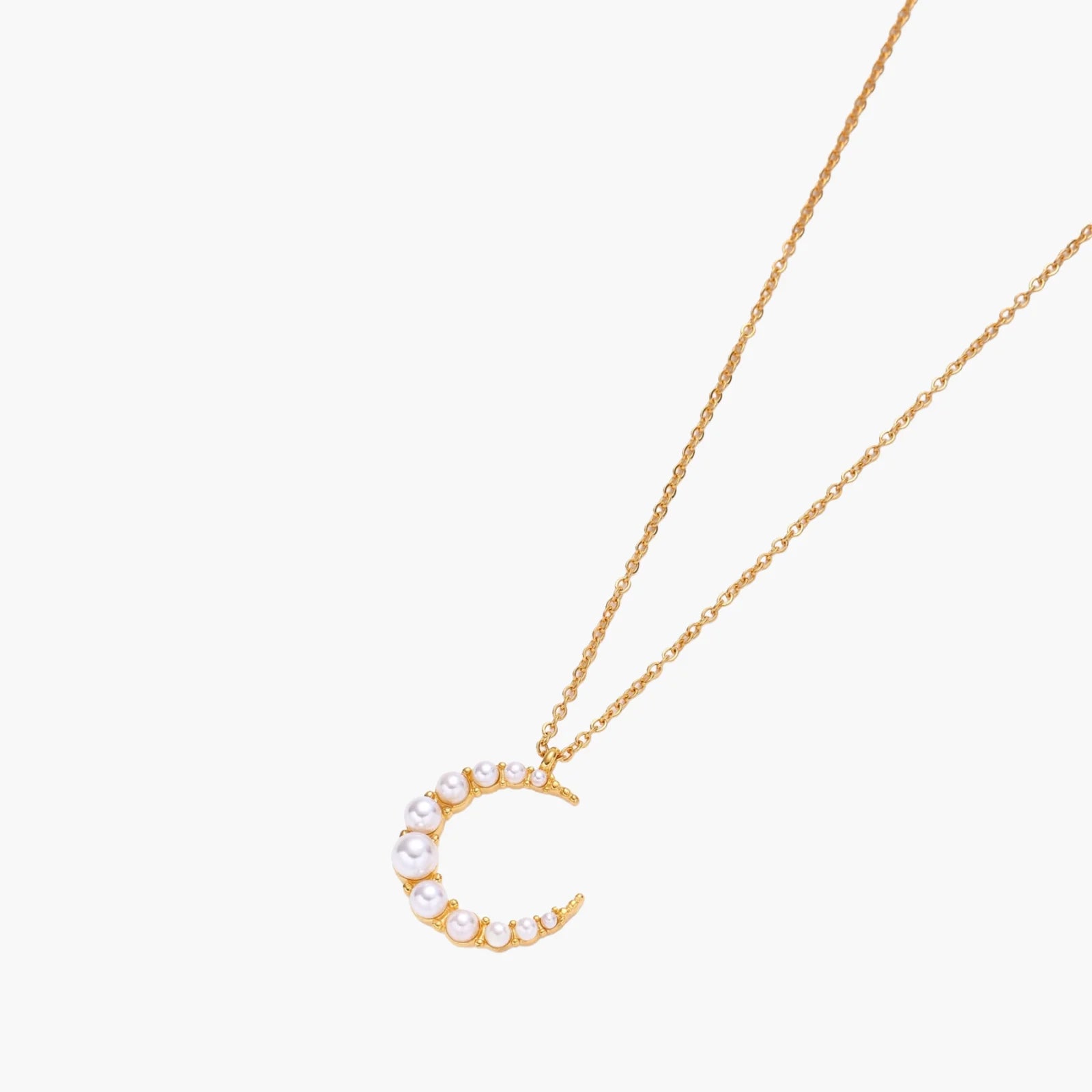 Gold crescent moon pendant with graduated white pearls on delicate chain against cream background