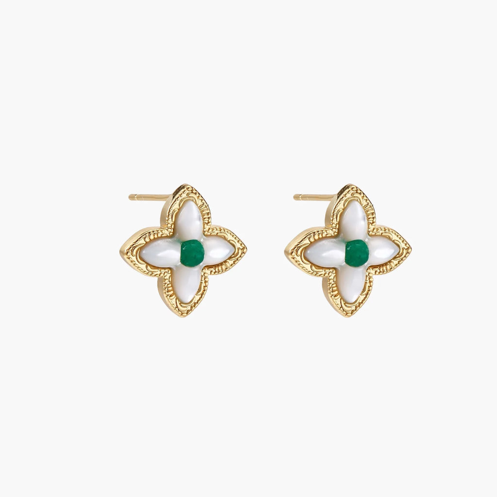 Gold quatrefoil stud earrings with white mother-of-pearl petals and emerald green gemstone center on beige background.
