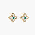 Gold quatrefoil stud earrings with white mother-of-pearl petals and emerald green gemstone center on beige background.