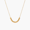 Delicate gold-plated necklace with graduated spherical beads forming gentle smile curve on beige background