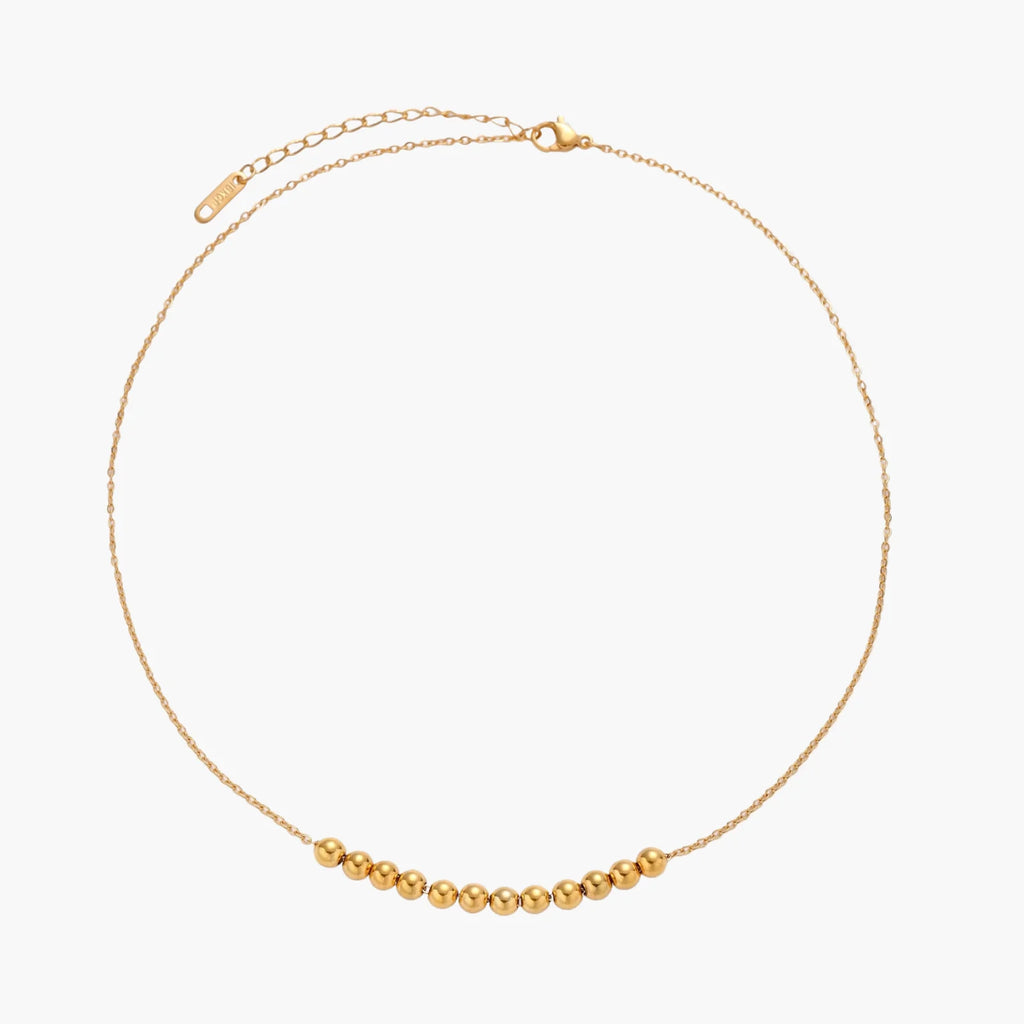 Delicate gold-plated necklace with graduated spherical beads forming gentle smile curve on beige background