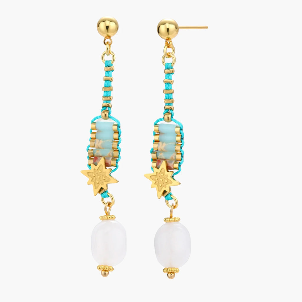 Gold-plated dangle earrings with turquoise threading, star charms, and white pearl beads against cream background.