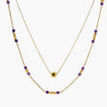 Two layered gold-tone necklaces with purple stone beads and star pendant against cream background.