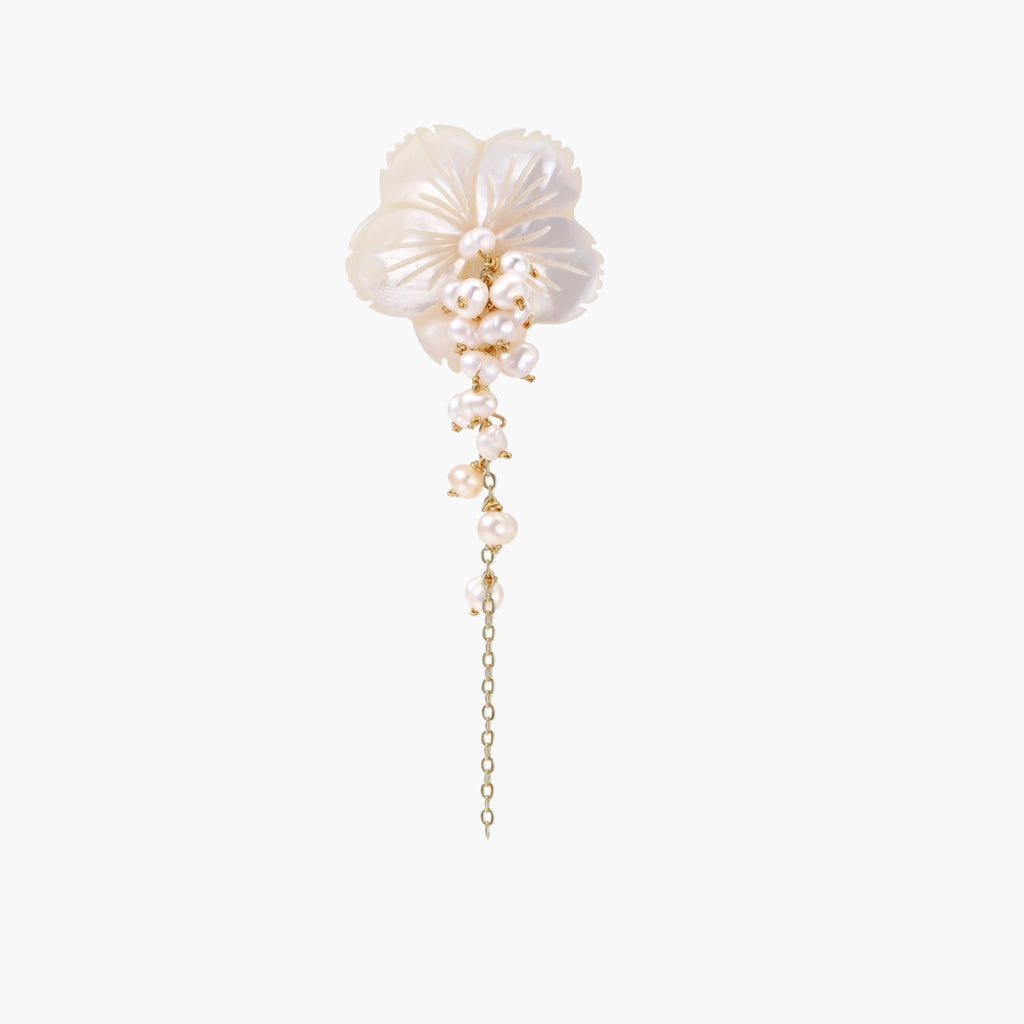 Iridescent shell flower brooch with carved petals and cascading freshwater pearls on gold chain against cream background.