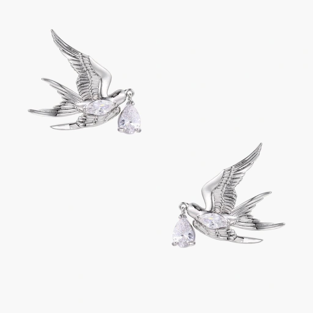Silver-toned swallow stud earrings with detailed wings carrying teardrop zirconia crystals on white background