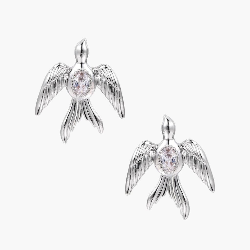 White gold-plated bird earrings with spread wings and oval zirconia center on cream background