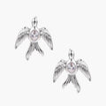 White gold-plated bird earrings with spread wings and oval zirconia center on cream background