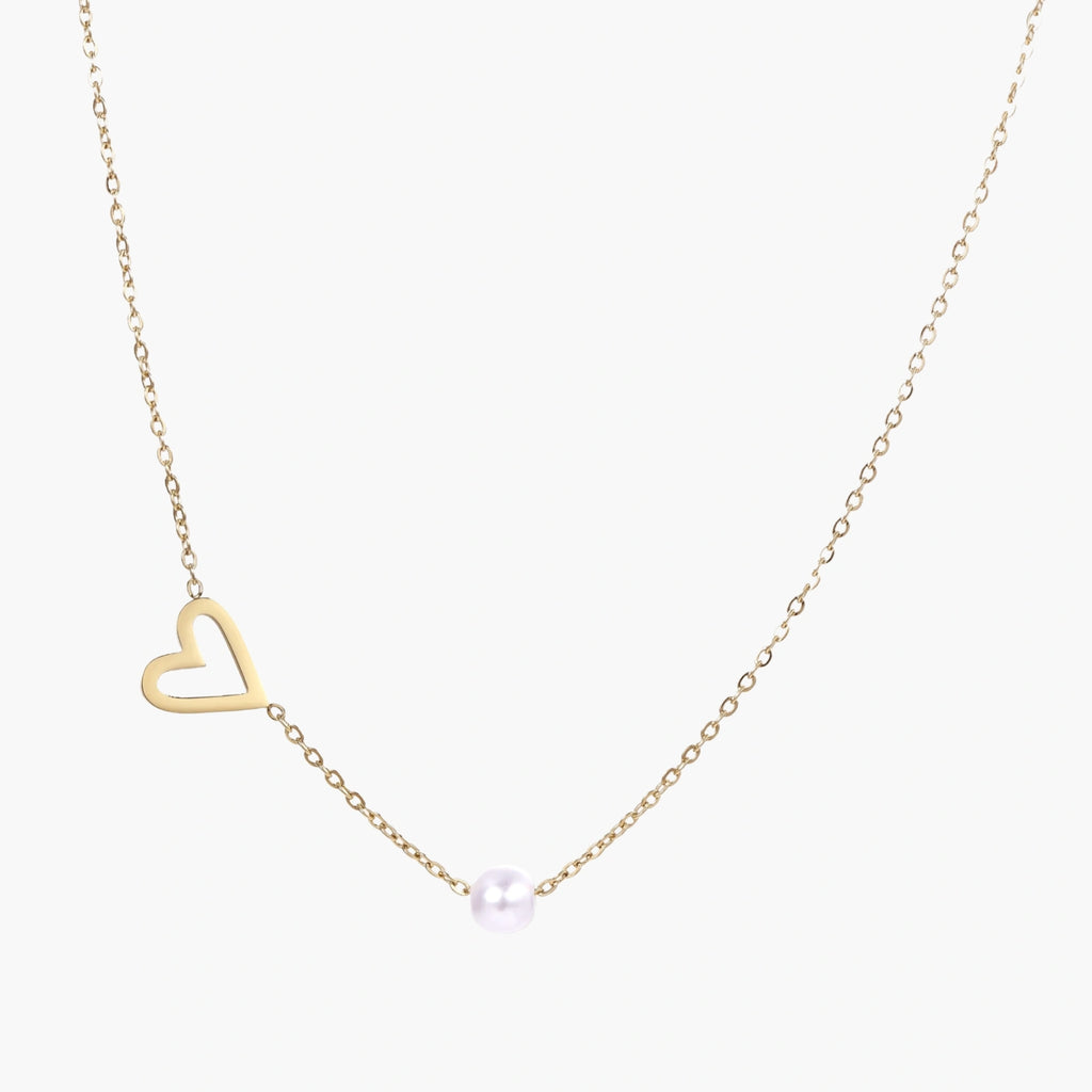 Delicate gold necklace with open heart charm and white pearl bead on fine chain against cream background