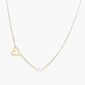 Delicate gold necklace with open heart charm and white pearl bead on fine chain against cream background
