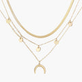 Four-layer gold necklace with herringbone chain, disc charms, and crescent moon pendant on cream background