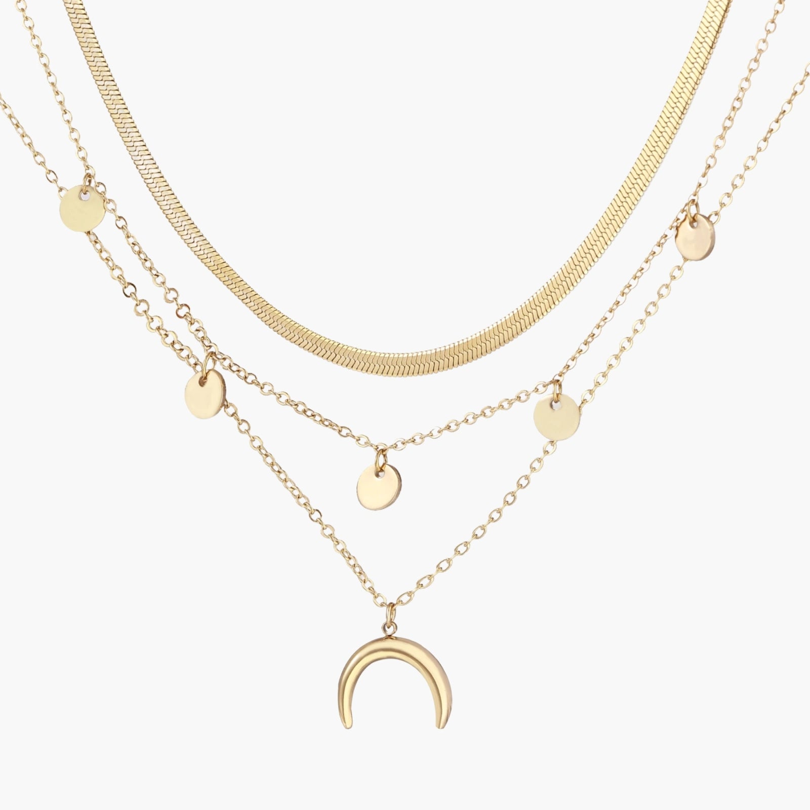 Four-layer gold necklace with herringbone chain, disc charms, and crescent moon pendant on cream background