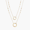 Layered gold necklace set with two open circle pendants and mixed chain styles on beige background