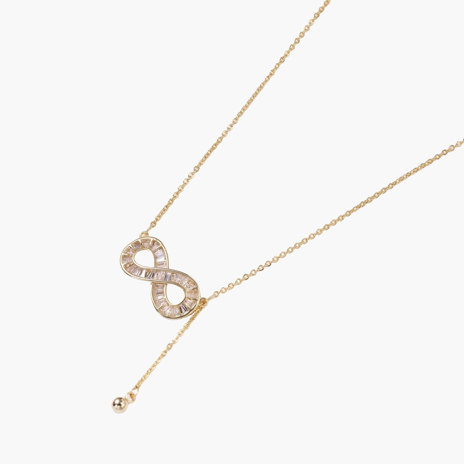 Gold infinity pendant with baguette crystals on adjustable chain against cream background.