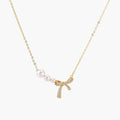 Delicate gold necklace with three white pearls and crystal-embellished bow pendant on cream background
