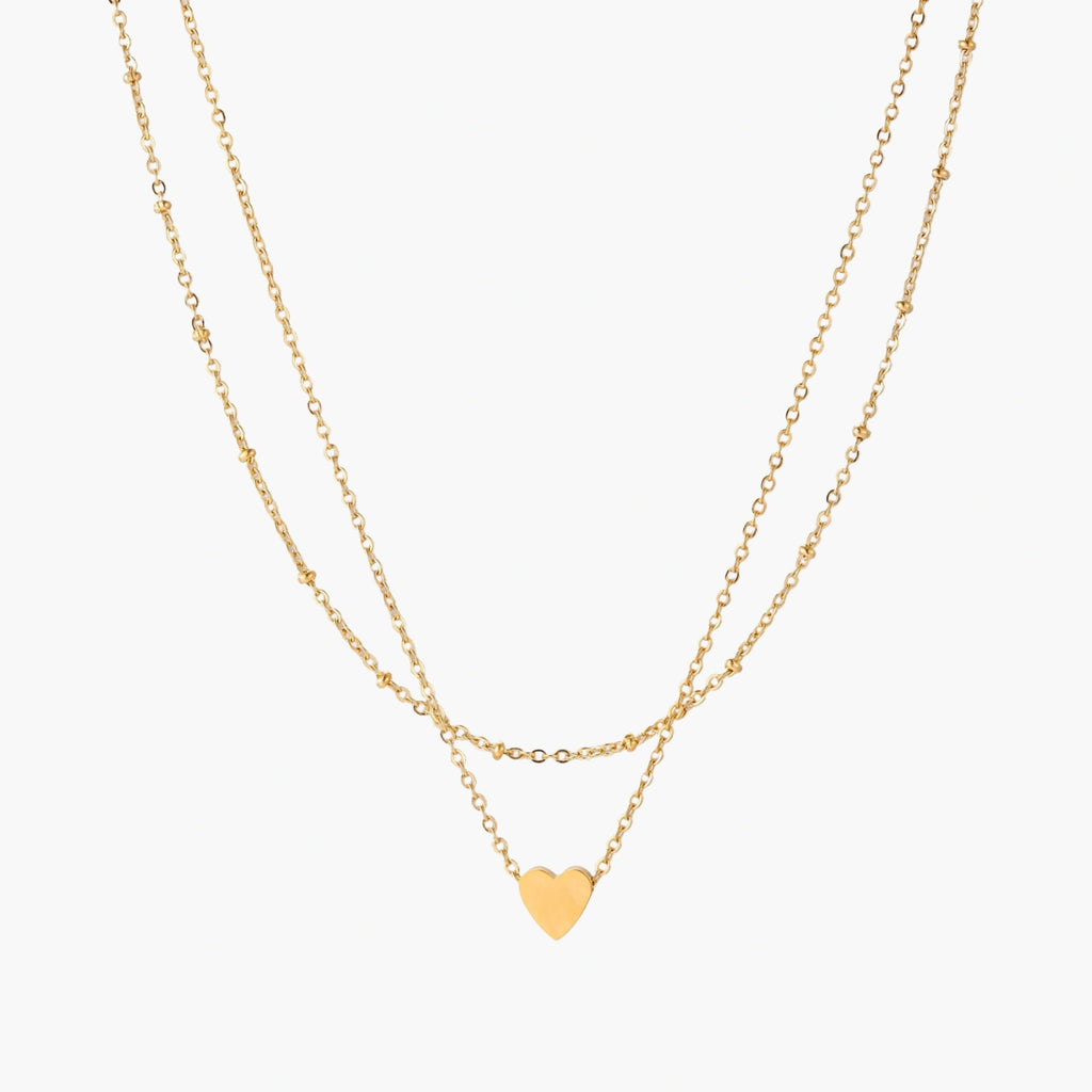 Delicate double-chain gold necklace with tiny heart pendant on cream background