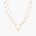 Delicate double-chain gold necklace with tiny heart pendant on cream background
