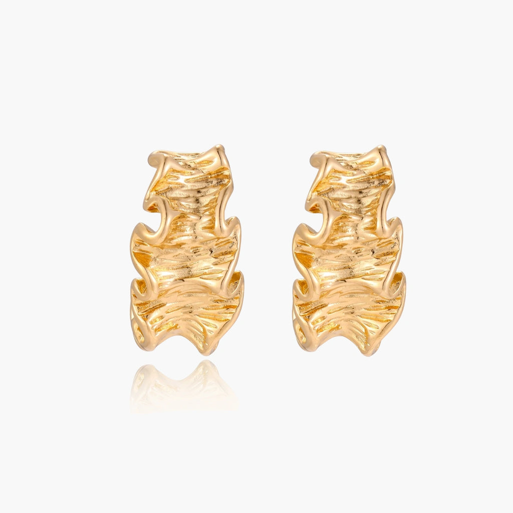 Pair of gold huggie hoops with sculpted wave texture and dimensional ripples on neutral background.