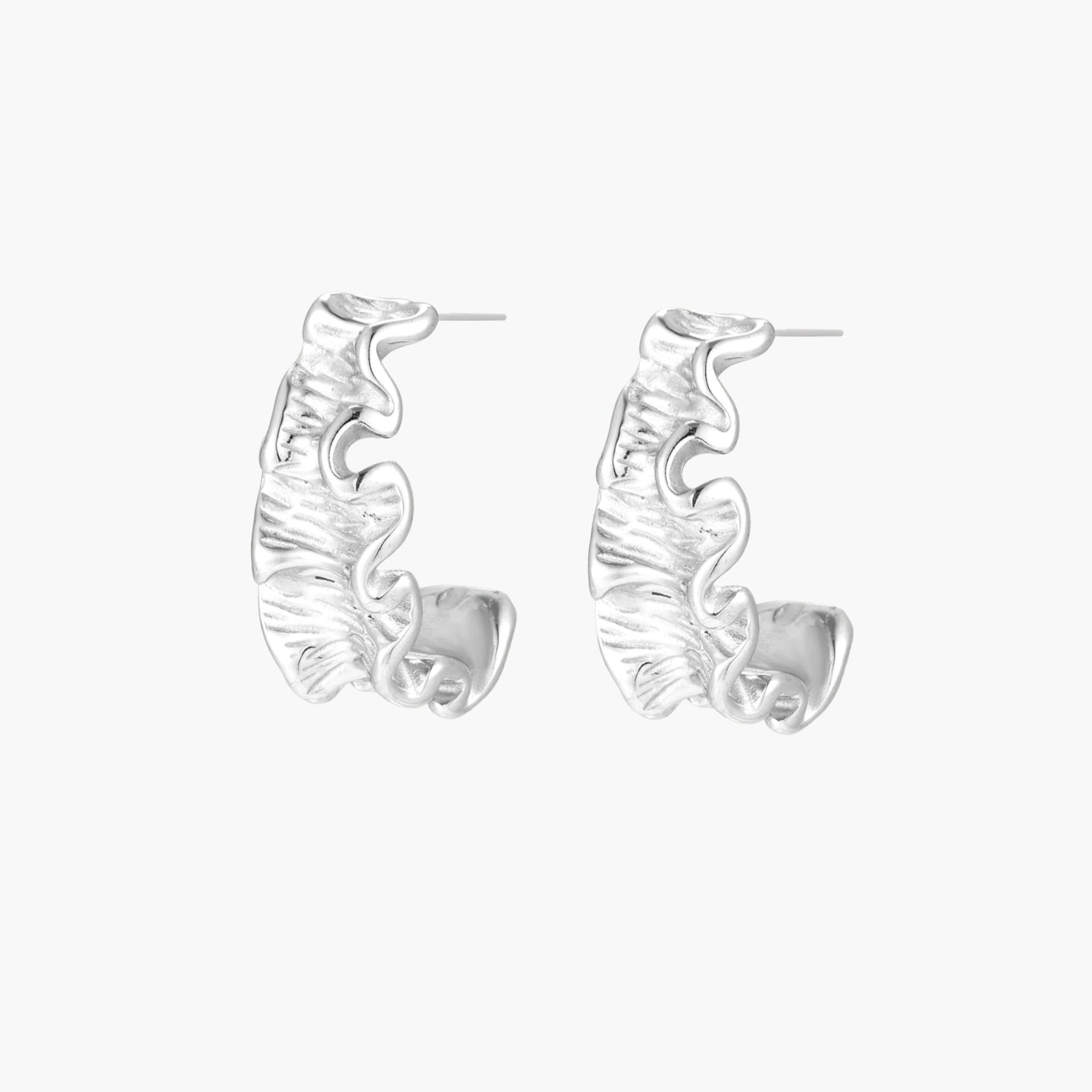 White gold plated sculptural hoop earrings with organic wavy edges and reflective metallic finish on cream background