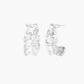 White gold plated sculptural hoop earrings with organic wavy edges and reflective metallic finish on cream background