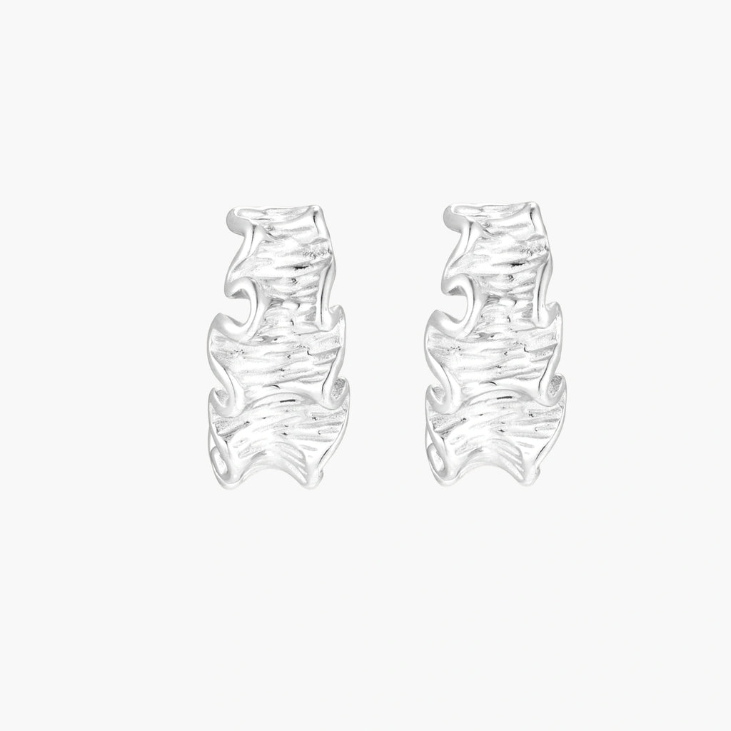 White gold plated sculptural hoop earrings with organic wavy edges and reflective metallic finish on cream background