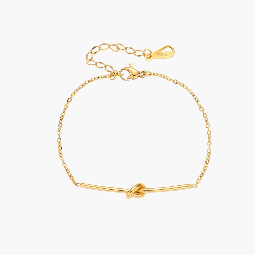Delicate gold chain bracelet with minimalist bar and centered knot detail on cream background