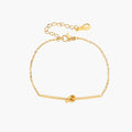 Delicate gold chain bracelet with minimalist bar and centered knot detail on cream background