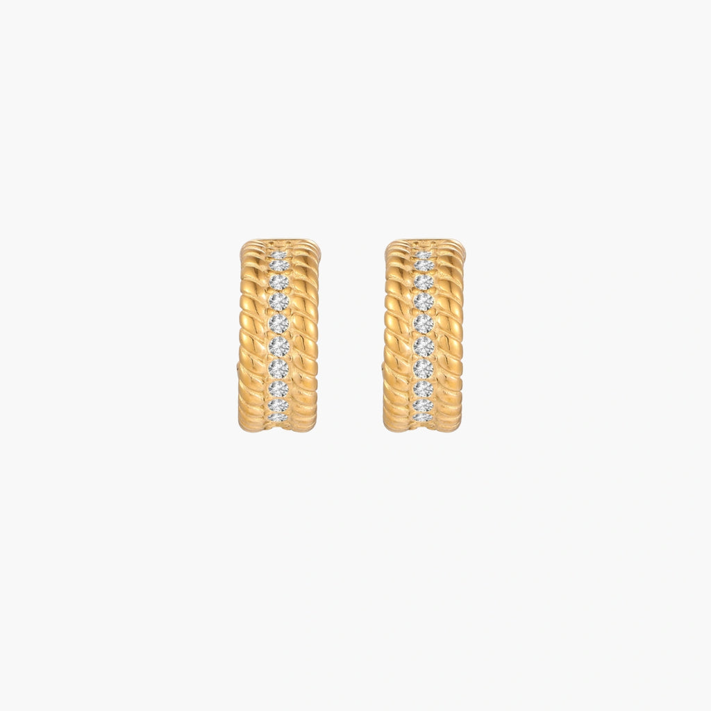 Textured gold huggie hoop earrings with raised ribbed rows creating dimensional sculptural design on cream background
